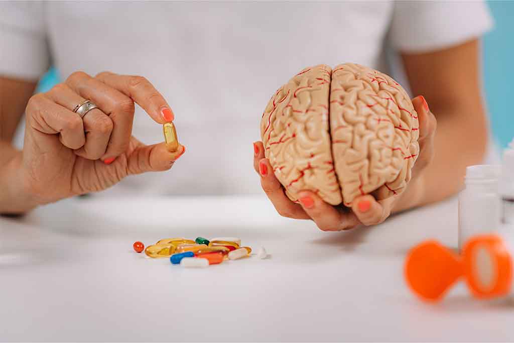Holding a pill in one hand and a mold of a brain in the other.